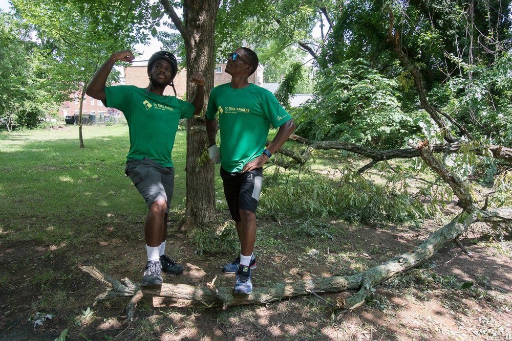 Two men in Trail Ranger shirts posing looking accomplished with a foot on a large tree branch. 
