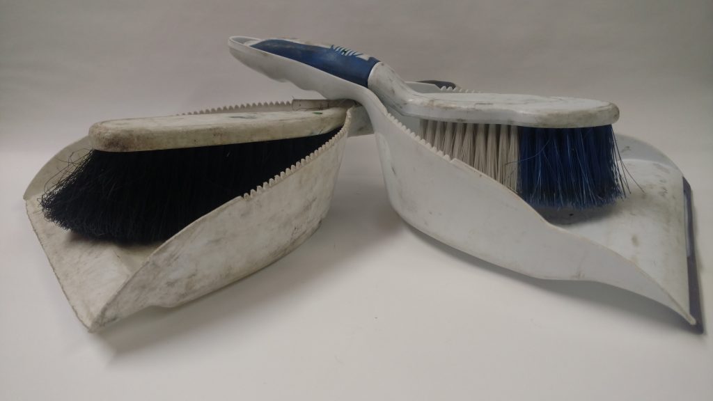 Glamor shot of two white dustpans and handbrooms on a white background. Both dustpans are used and dirty though the dustpan on the left is clearly more used. 