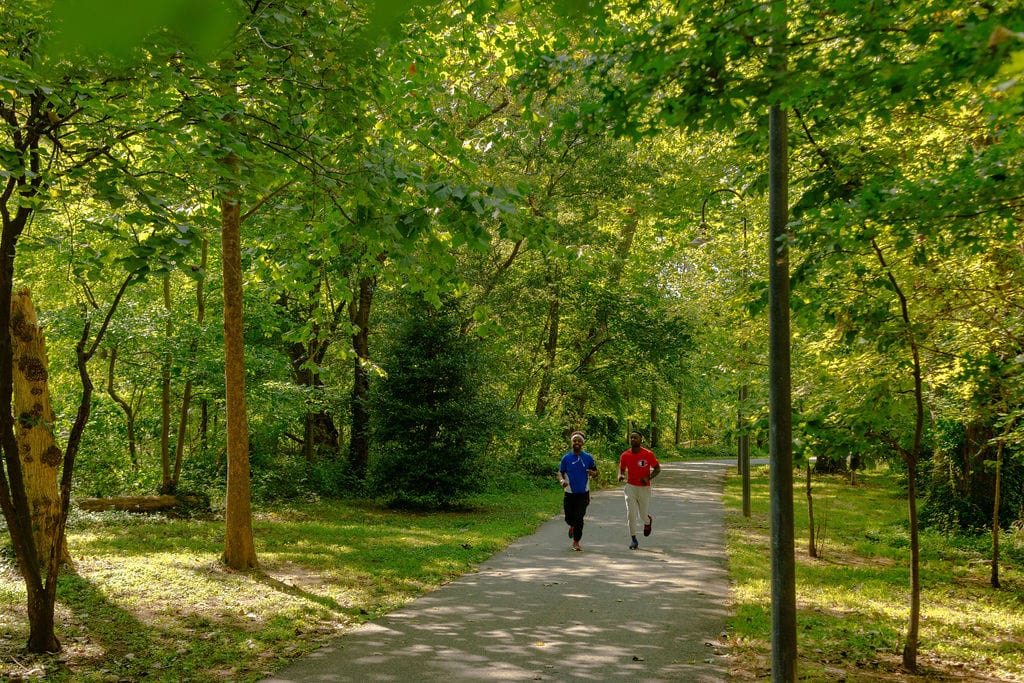 Two black guys are running towards the camera on a trail with vibrant greenery around them. Its Marvin Gaye Trail peak casual exercise and its excellent.