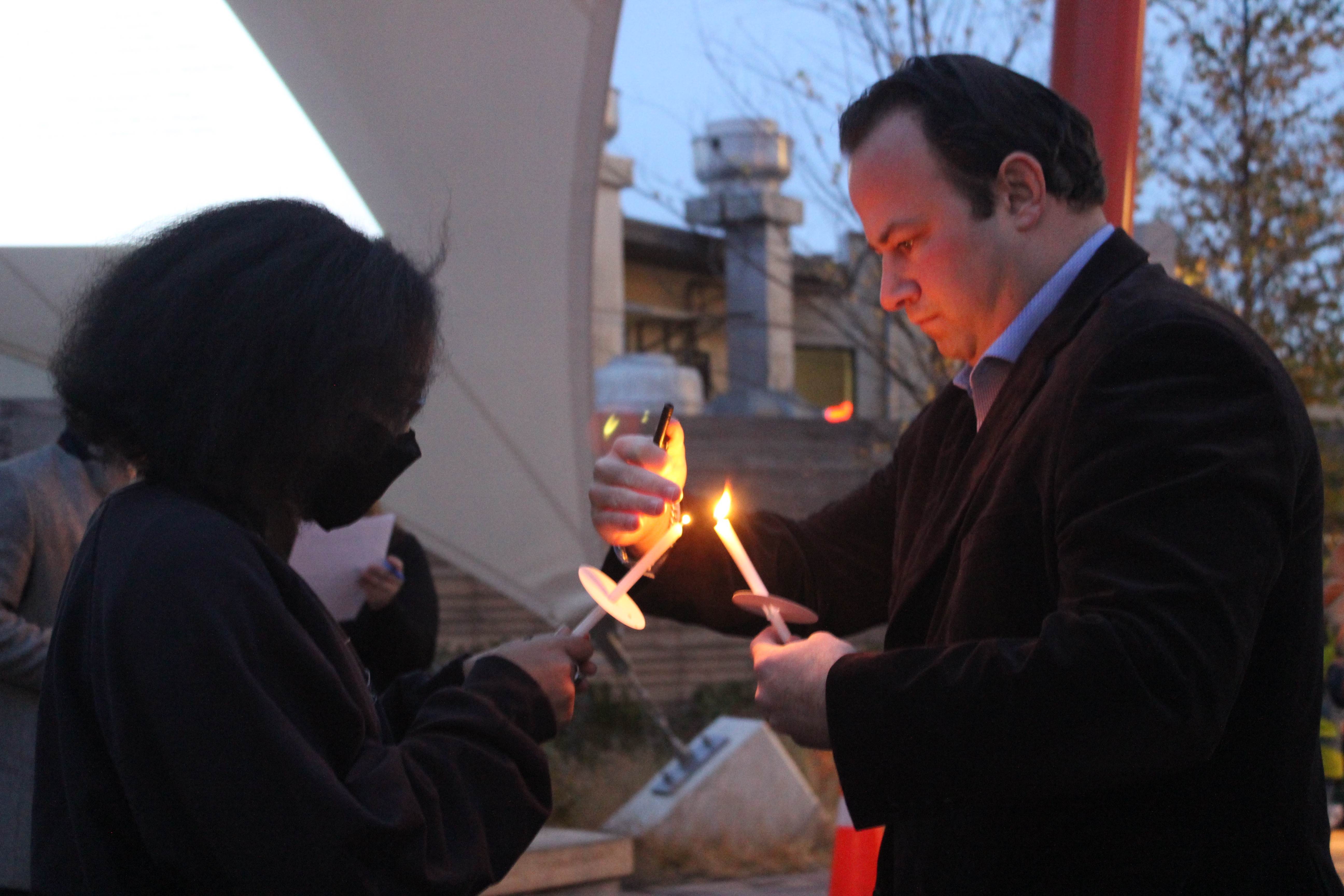 A woman holds a candle out for a man to lights another one from its flame.