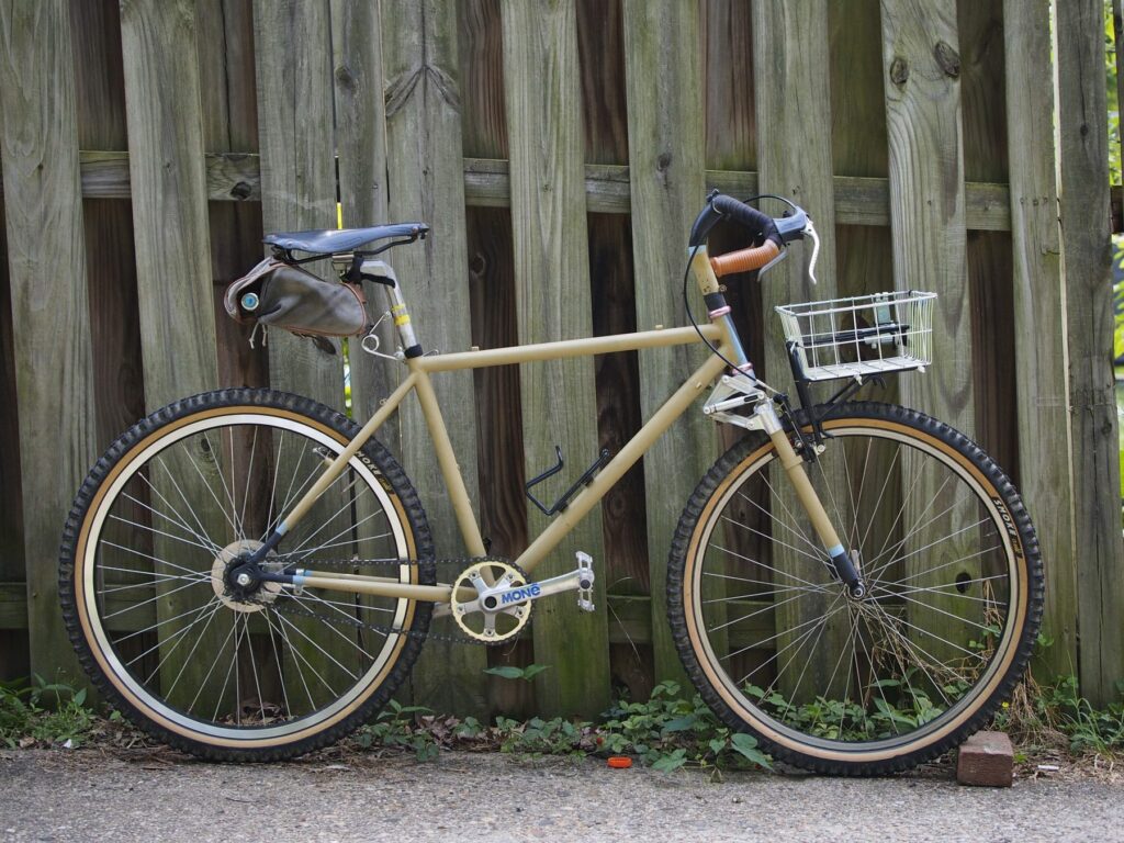 A tan bike with a wald basket on a small front rack.