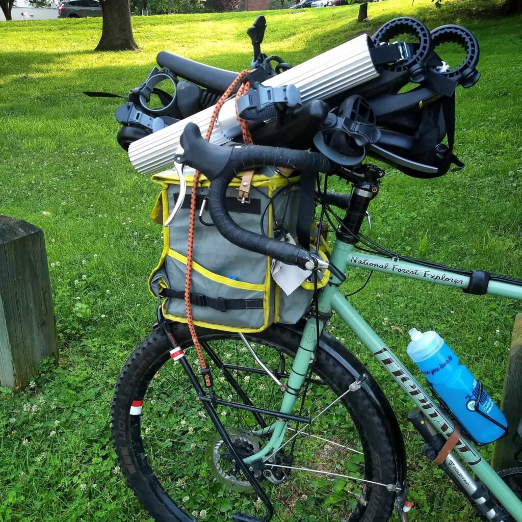 A green bike with a car-bike rack bungeed to the top of a handlebar bag.