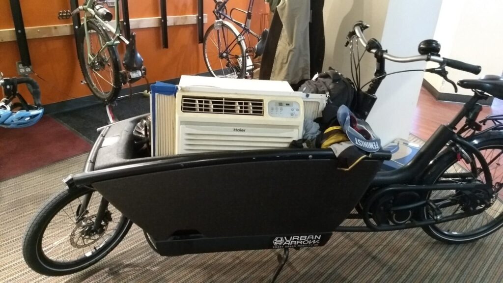 A black Urban Arrow box bike with an air conditioner in it. 